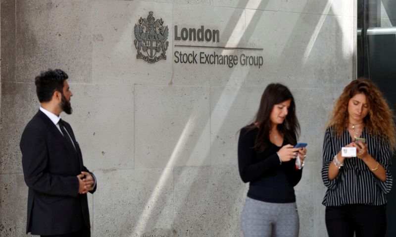 FILE PHOTO: People check their mobile phones as they stand outside the entrance of the London Stock Exchange in London