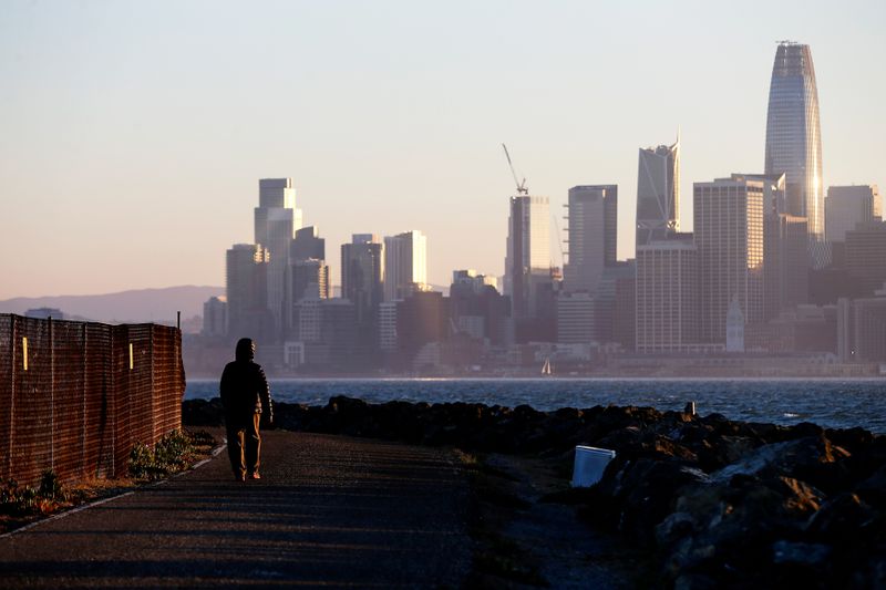 FILE PHOTO: The San Francisco skyline is seen behind a woman as she walks past a condemned area on Treasure Island, near San Francisco