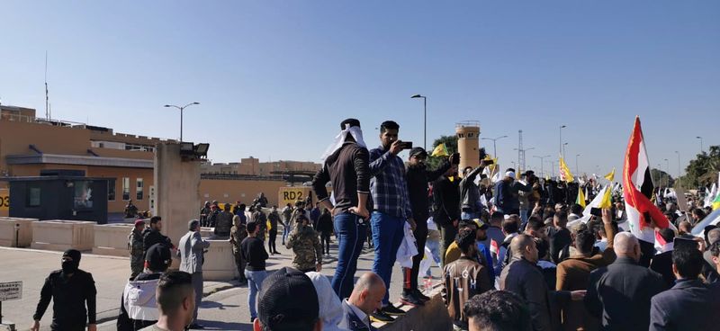Protesters and militia fighters gather to condemn air strikes on bases belonging to Hashd al-Shaabi, outside the main gate of the U.S. Embassy in Baghdad