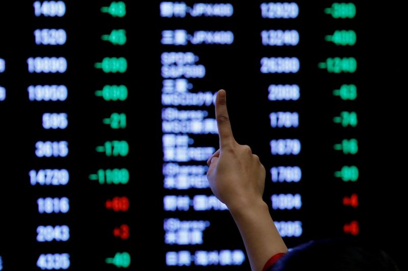 FILE PHOTO: A woman points to an electronic board showing stock prices as she poses in front of the board after the New Year opening ceremony at the Tokyo Stock Exchange (TSE), held to wish for the success of Japan's stock market, in Tokyo