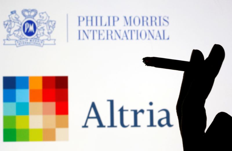 A hand with a cigarette is seen in front of displayed logos of Philip Morris and Altria in this picture illustration