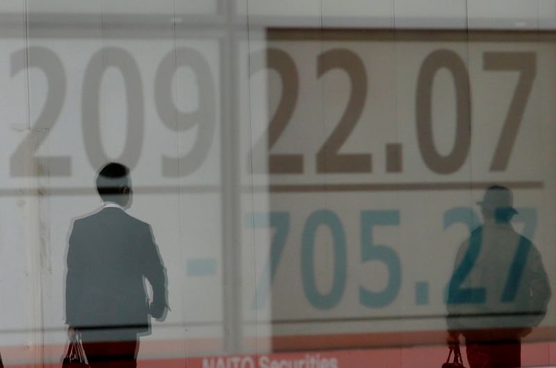 FILE PHOTO: Men are reflected on an electronic board showing the Nikkei stock index outside a brokerage in Tokyo