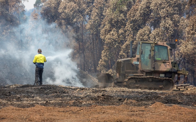 An Australian Army combat engineer from the 5th Engineer Regiment utilises a JD-450 Bulldozer to spread out burnt woodchip at the Eden Woodchip Mill in southern New South Wales