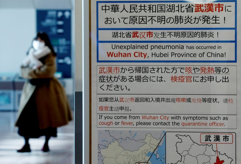 FILE PHOTO: A woman wearing a mask walks past a quarantine notice about the outbreak of coronavirus in Wuhan, China at an arrival hall of Haneda airport in Tokyo