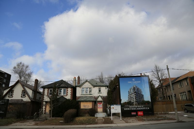 A real estate assembly of houses marked for demolition stand next to a billboard advertising a future condominium in Toronto