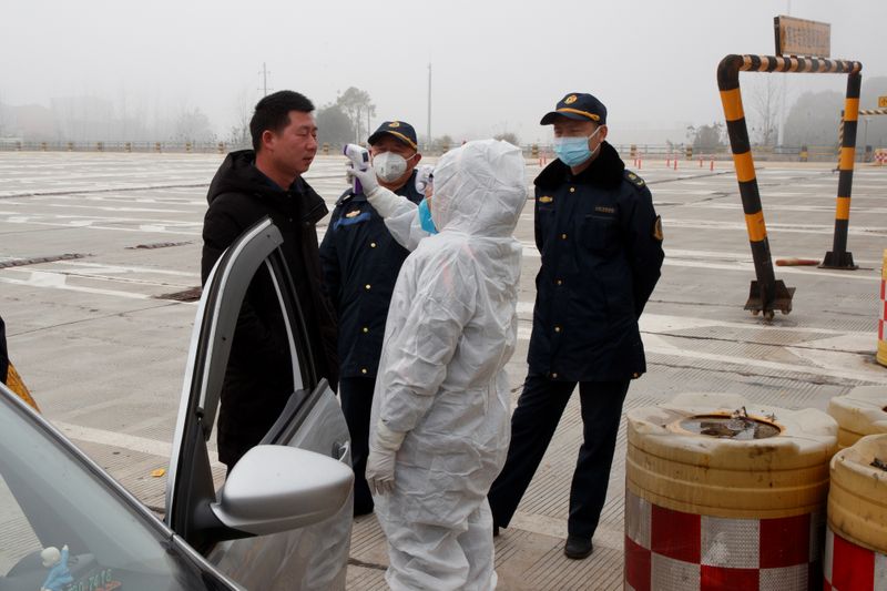 A medical worker in protective suit checks the body temperature of a driver at a checkpoint outside the city of Yueyang