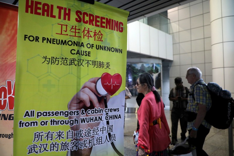 FILE PHOTO: Passengers pass a banner about Wuhan Pneumonia at a thermal screening point in the international arrival terminal of Kuala Lumpur International Airport in Sepang