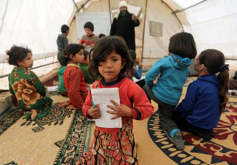 A student holds a notebook as she sits at a makeshift school in a tent in Azaz