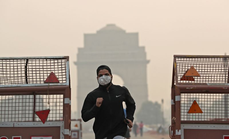 FILE PHOTO: A man wearing a mask runs past the India Gate on a smoggy morning in New Delhi