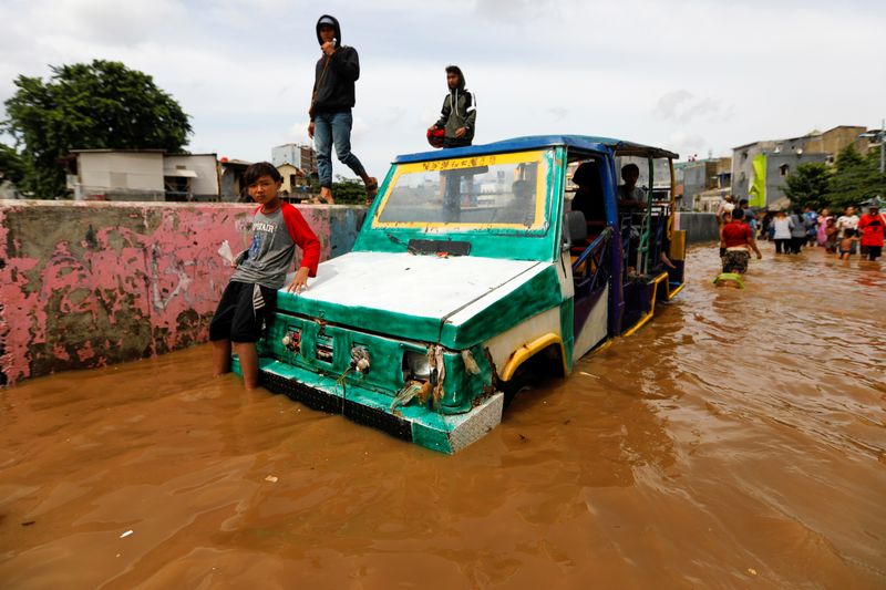 Youth sits on a car at an area flooded after heavy rains in Jakarta