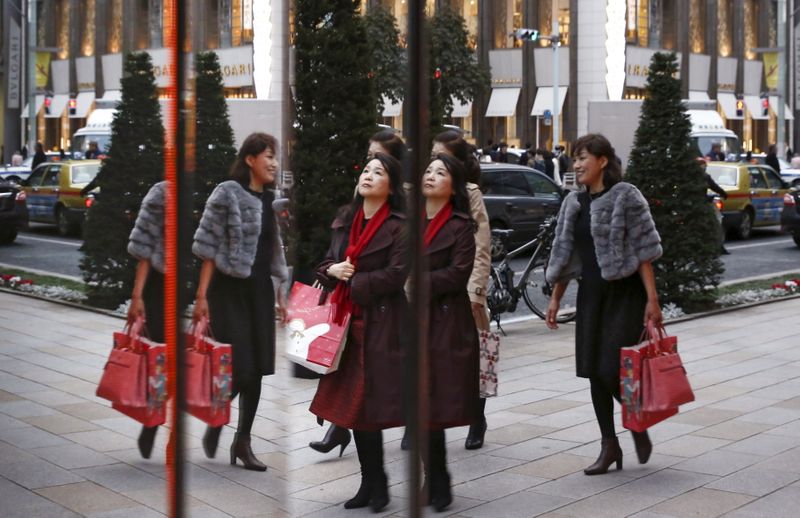 Women are reflected in a window as they pass a boutique in a shopping district in Tokyo