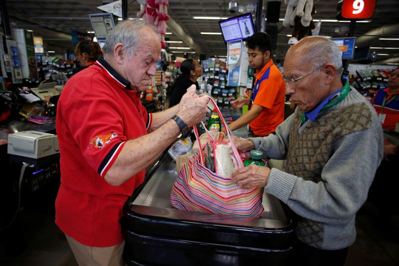An employee helps a man to arrange groceries in a bag at a supermarket which no longer provides plastic bags for customers to carry products, in Mexico City