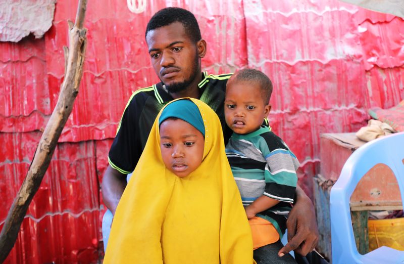 Somali farmer Abdi Abukar Hassan sits with his son and daughter during a Reuters interview outside his house in Mogadishu