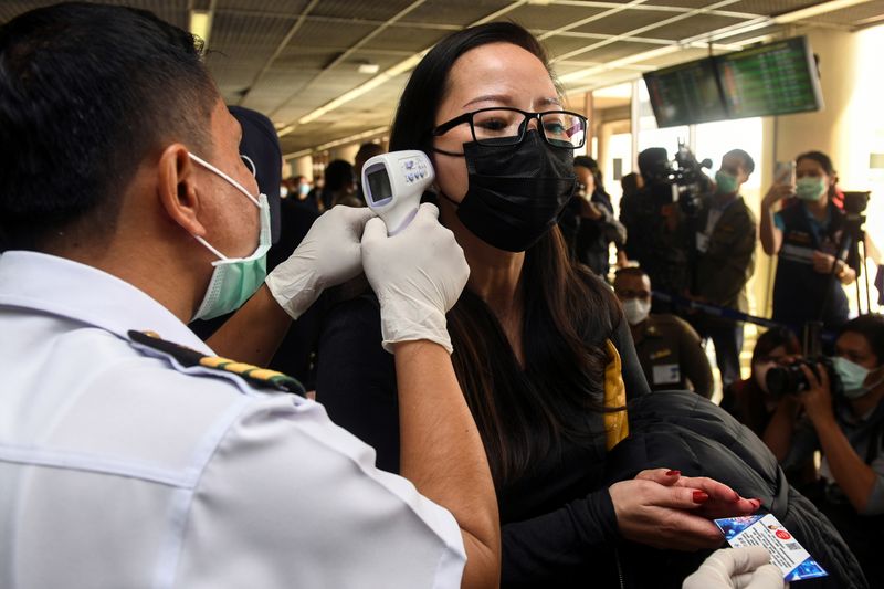 A health worker uses an infrared thermometer to check the temperature of a tourist who arrives at Bangkok's Don Mueang Airport