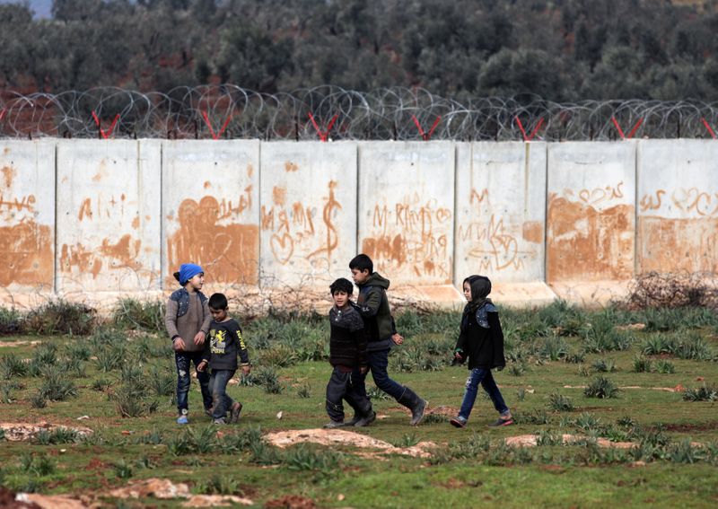 Internally displaced boys walk near the wall in Atmah IDP camp, located near the border with Turkey