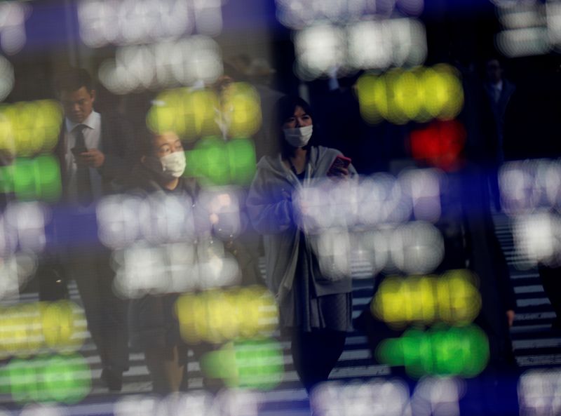 Pedestrians wearing facial masks are reflected on an electric board showing stock prices outside a brokerage at a business district in Tokyo