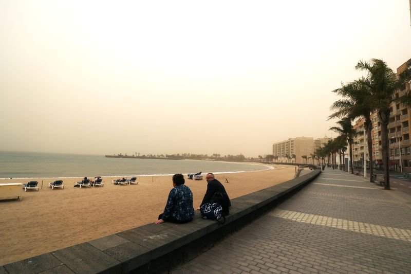 People look over the sea into the haze created by a sand storm known locally as 