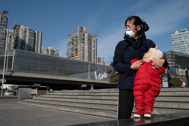 Woman wearing a face mask holds a child near a shopping mall in Beijing