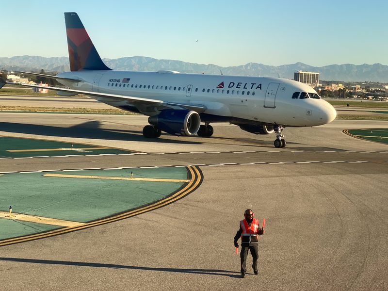 An airport worker guides a Delta Air Lines Airus A319 plane on the tarmac at LAX in Los Angeles
