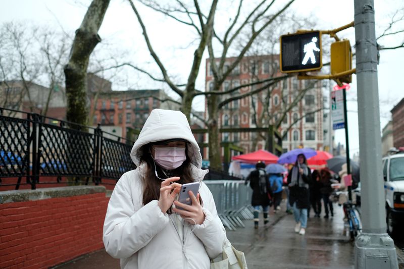 Woman with a face mask looks at her phone in Chinatown in New York City