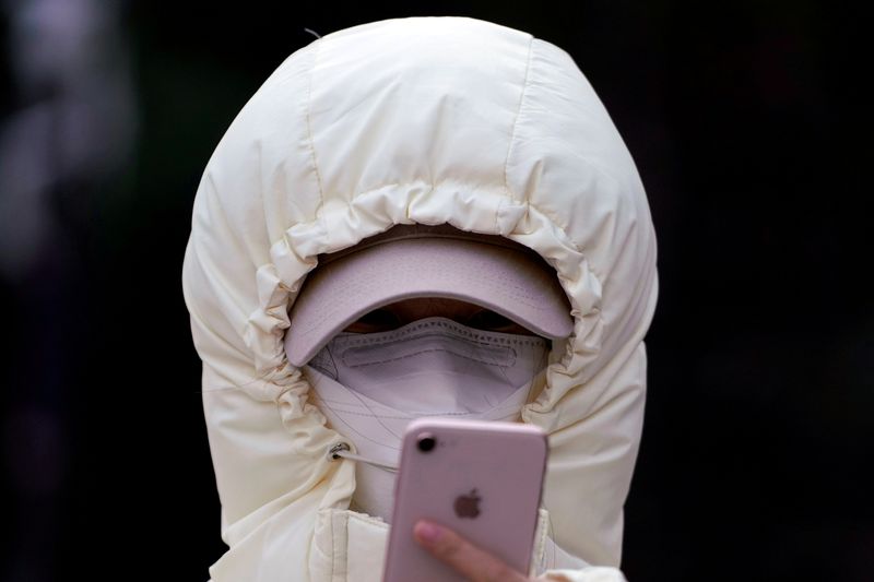 FILE PHOTO: A woman wearing a mask checks her mobile phone in Shanghai
