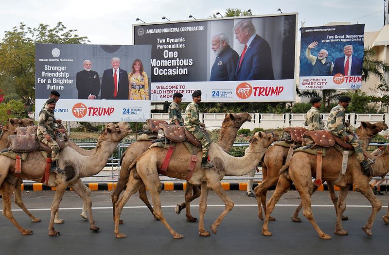 BSF soldiers ride their camels past hoardings with the images of India's Prime Minister Narendra Modi, U.S. President Donald Trump and first lady Melania Trump, as they take part in a rehearsal for a road show ahead of Trump's visit, in Ahmedabad