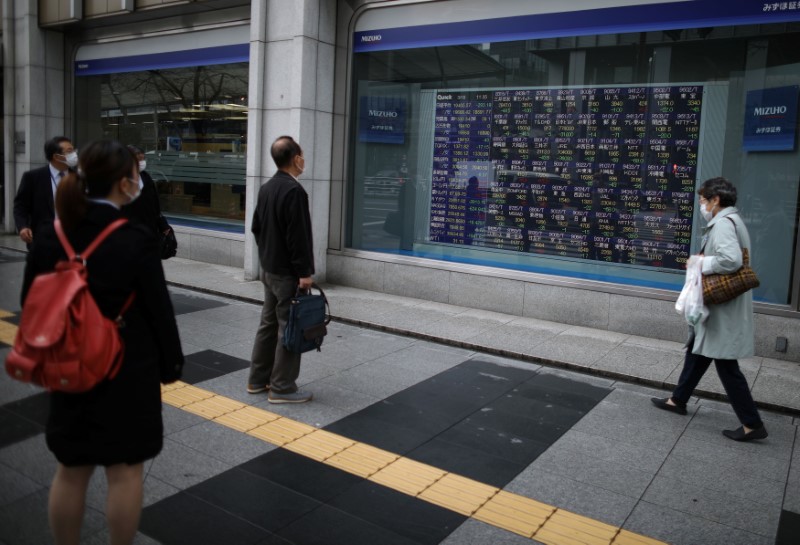 People wearing protective face masks look at a stock quotation board outside a brokerage in Tokyo