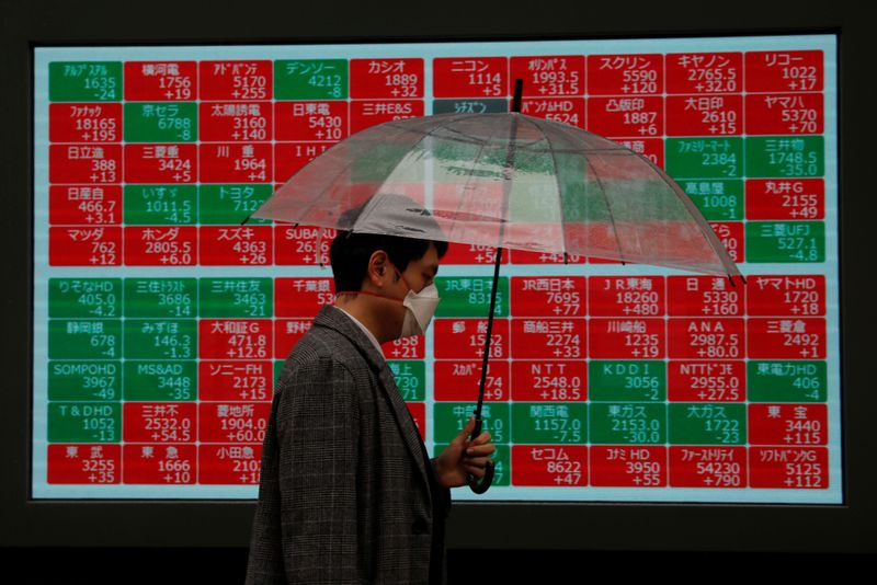 A visitor wearing protective face mask, following an outbreak of the coronavirus, walks past in front of a stock quotation board outside a brokerage in Tokyo