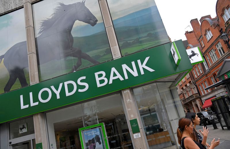 FILE PHOTO: A woman looks at her phone as she walks past a branch of Lloyds bank in London, Britain