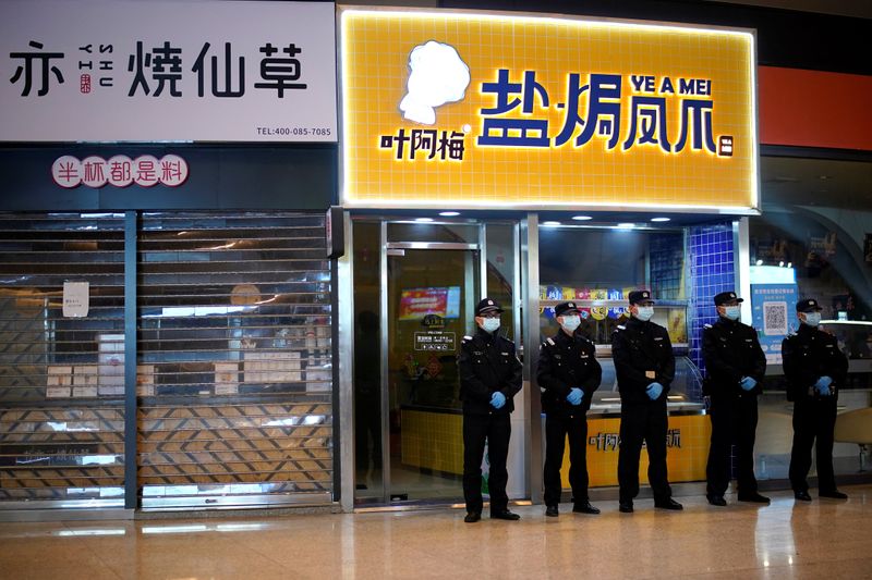 Security personnel wearing face masks stand guard in front of closed shops inside a railway station in Wuhan