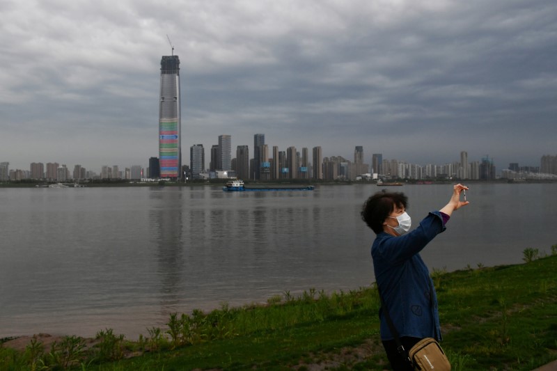 Woman wearing a face mask takes pictures with a mobile phone at a riverside park in Wuhan