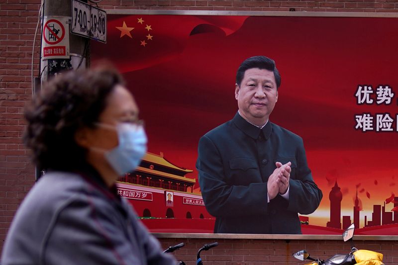 A woman wearing a protective mask is seen past a portrait of Chinese President Xi on a street as the country is hit by an outbreak of the coronavirus, in Shanghai