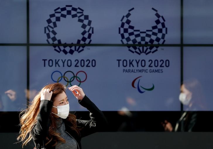 A passerby wearing a protective face mask following an outbreak of the coronavirus disease (COVID-19) walks past a screen displaying logos of Tokyo 2020 Olympic and Paralympic Games in Tokyo