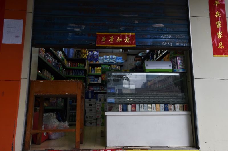 Man wearing a face mask stands inside a shop with the roller shutter half closed, in Wuhan, the epicentre of the novel coronavirus outbreak