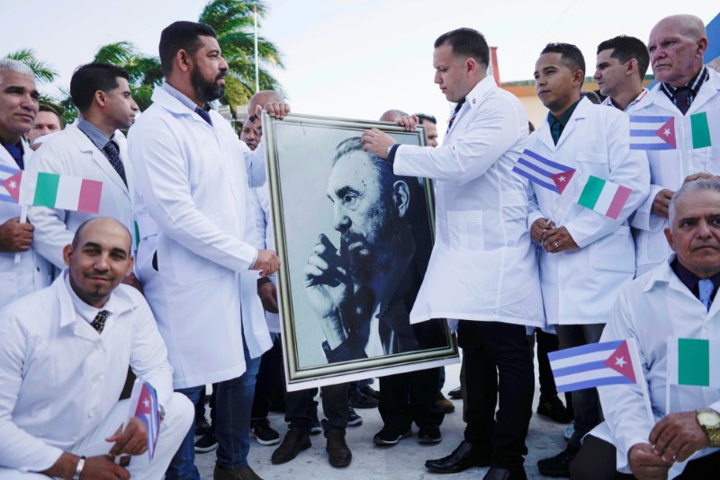 Cuban doctors hold an image of late Cuban President Fidel Castro during a farewell ceremony before departing to Italy to assist, amid concerns about the spread of the coronavirus disease (COVID-19) outbreak, in Havana