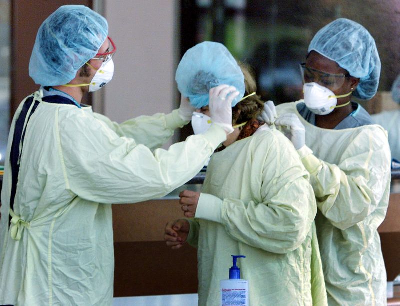 FILE PHOTO: HOSPITAL WORKERS HELP A VISITOR PUT ON CLOTHING TO PROTECT AGAINSTSARS.