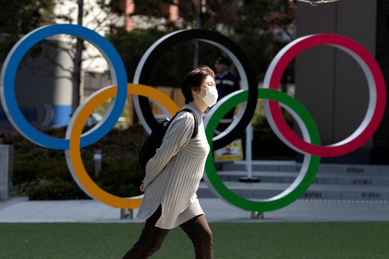 FILE PHOTO: A woman wearing a protective face mask, following an outbreak of the coronavirus disease (COVID-19), walks past the Olympic rings in front of the Japan Olympics Museum in Tokyo