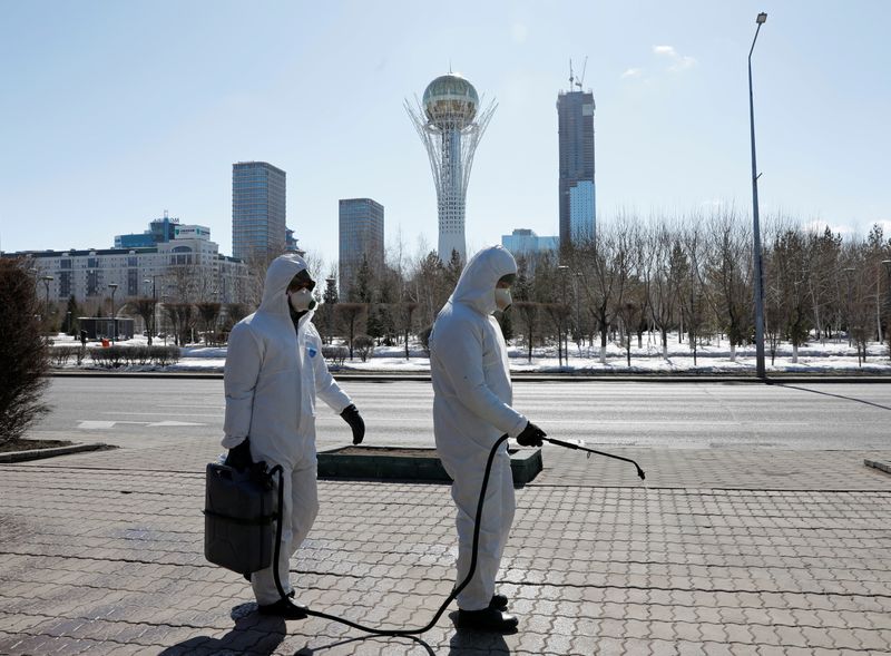 Workers wearing protective suits spray disinfectant on the street in Nur-Sultan