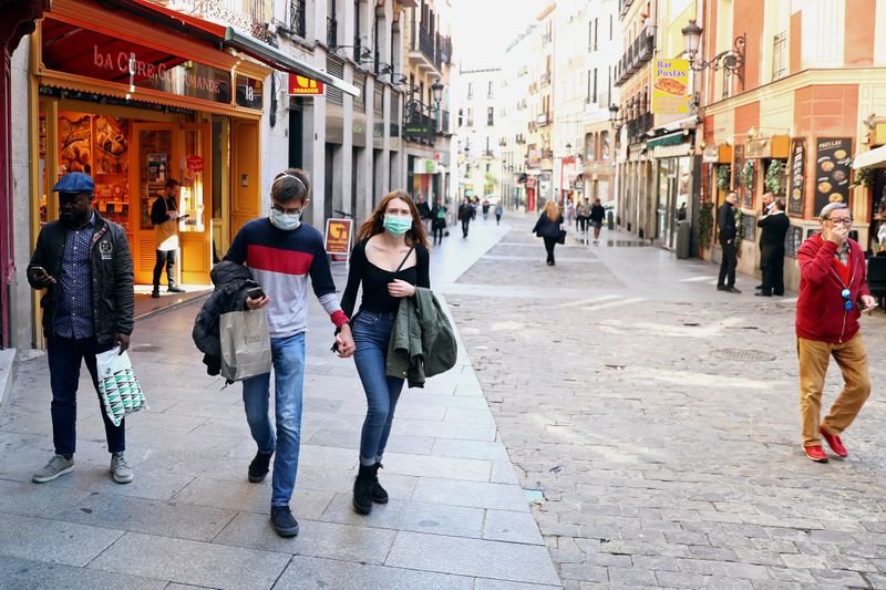 A couple wear protective face masks as they walk in unusually quiet Postas street in central Madrid
