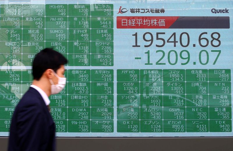 A passerby wearing a protective face mask walks past an electronic display outside a brokerage in Tokyo