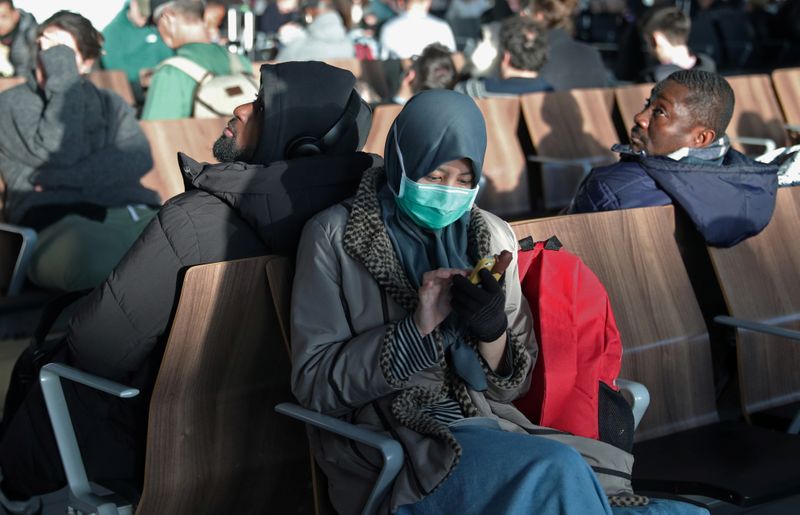A woman wears a surgical mask as she sits in Terminal 5 at Heathrow Airport in London