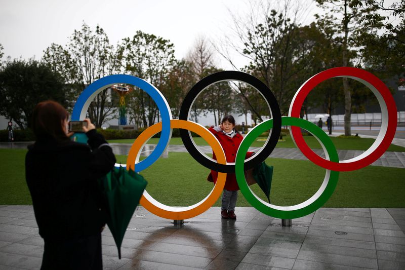 A woman poses for a photo through The Olympic rings in front of the Japan Olympics Museum in Tokyo