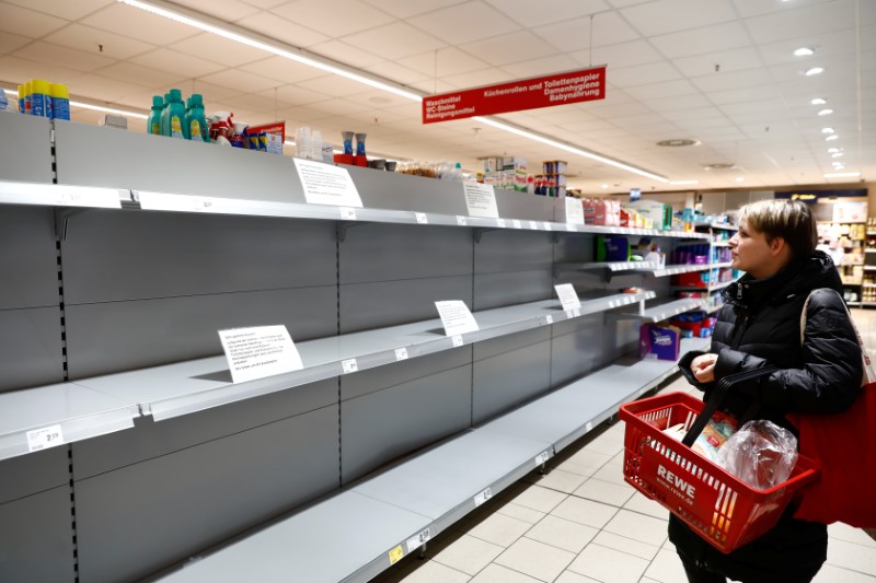 FILE PHOTO: A woman looks at an empty shelf with a sign announcing the rationing of toilet paper at a Rewe grocery store in Potsdam