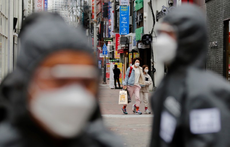 Pedestrians wearing masks are seen behind South Korean soldiers doing quarantine works, following the rise in confirmed cases of coronavirus disease (COVID-19) in Daegu