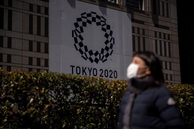 A woman wearing a protective face mask, following an outbreak of the coronavirus, walks past a banner for the upcoming Tokyo 2020 Olympics in front of the Tokyo Metro Government building in Tokyo