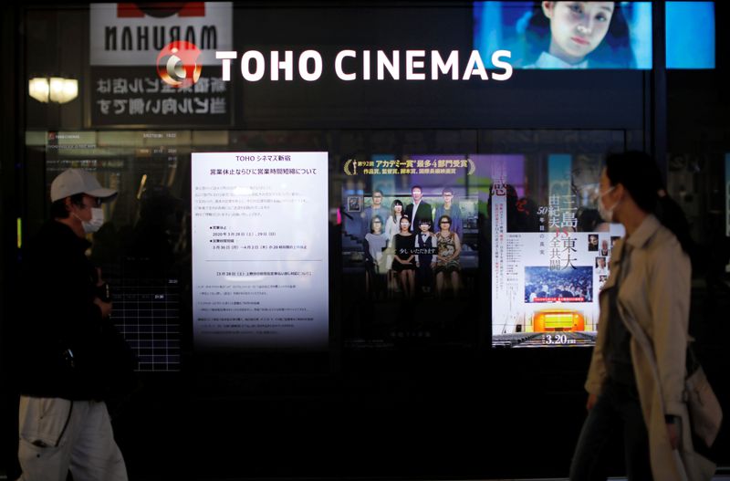FILE PHOTO: Passersby wearing protective face masks walk past notices of closed and business hours reduction displayed in front of a movie theater in Tokyo