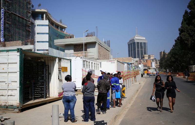 Women walk past job seekers outside a construction site in Sandton, an affluent area situated within the metro of Johannesburg