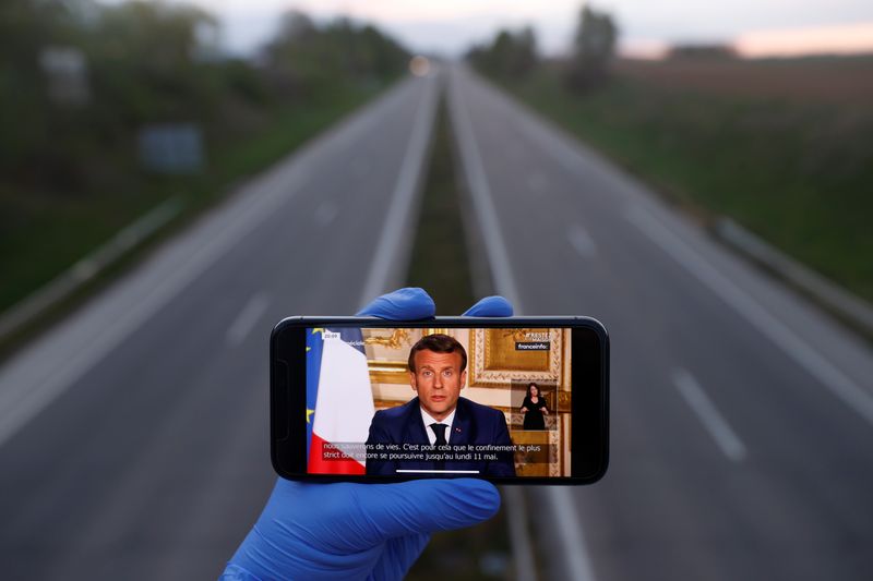 A mobile phone showing French President Emmanuel Macron, as he addresses the nation about the coronavirus disease (COVID-19) outbreak is displayed for a phot in front of an almost empty motorway in Strasbourg