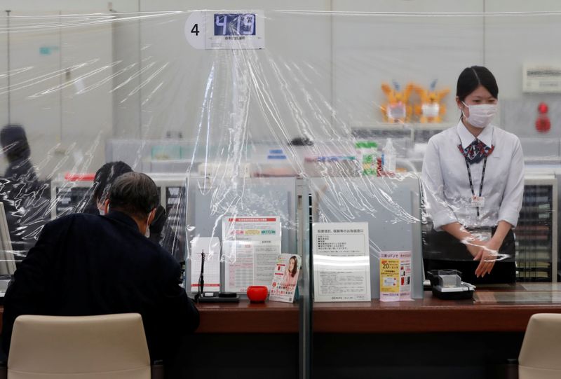 A bank teller wearing a protective face mask stands at a counter where a plastic curtain is installed in order to prevent infections following the coronavirus disease (COVID-19) outbreak, at the Higashinakano branch of MUFG Bank in Tokyo