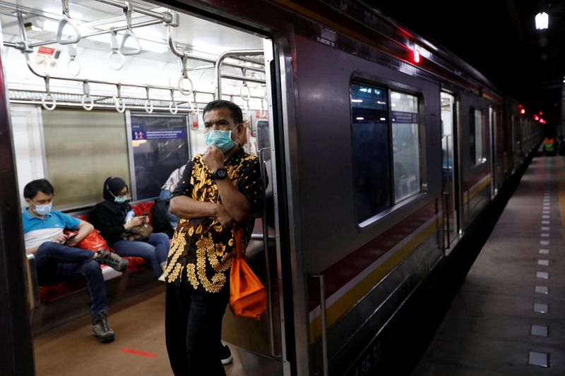 Man wearing a protective mask stands inside a commuter train during the imposition of large-scale restrictions by the government to prevent the spread of coronavirus disease (COVID-19) in Jakarta